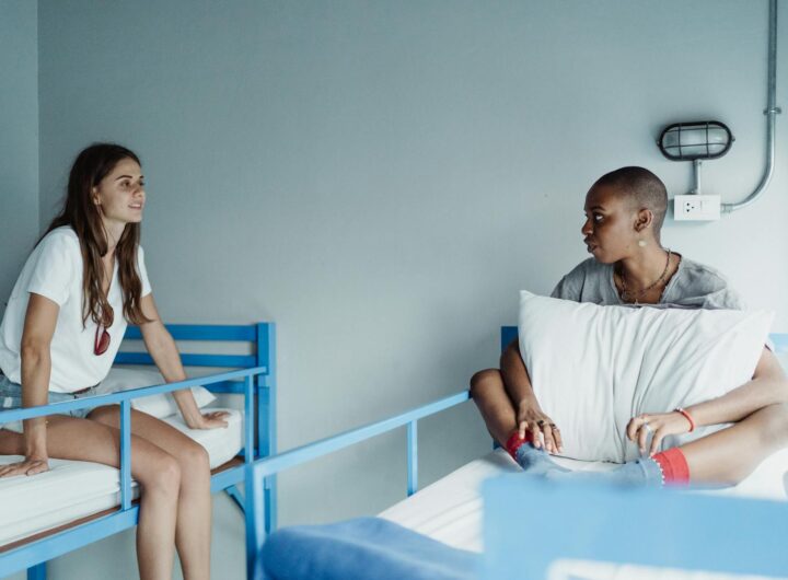 Deux femmes sont assises et discutent tranquillement sur des lits superposés dans une chambre d'auberge.
